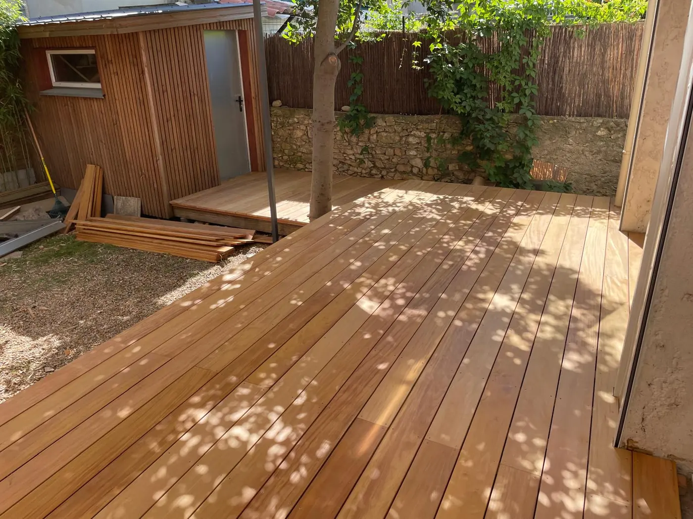 Terrasse en bois dans un jardin, devant un abri en bois